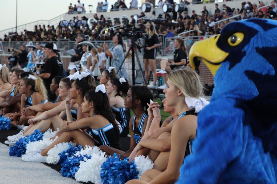 Cheerleaders and Blue Hawk Mascot, Rocky, watching athletes getting introduced on the field.