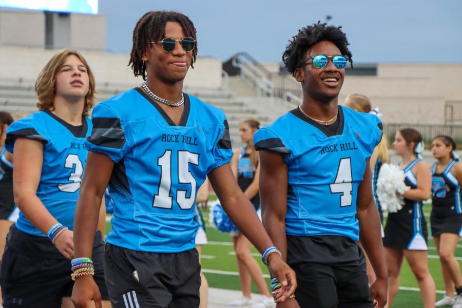 Sophomore Isaiah Orlandi and junior Amar Williams walk toward the crowd as the varsity football team is announced. "Just being with my friends and teammates and coaches every day [motivates me]," Williams said. Despite transitioning to a higher division, Williams hopes to have a winning record and make the playoffs this season.