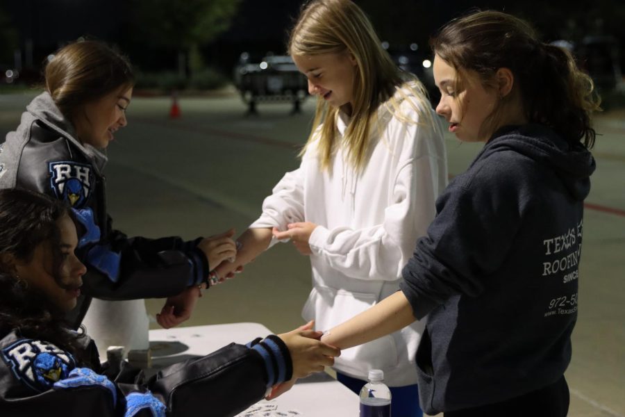 Students are shown in the photo receiving washable tattoos from two Rockettes, getting a taste of high school culture. 