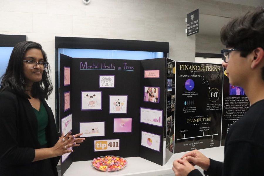 Giving out information to another former student, junior Debanshi Pattanaik (left), talks about the mental health of teenagers. "I feel like it’s pretty cool to be able to see everyone’s individual career interests, and all the work they’ve put throughout the year into their projects," junior Diego Bermudez said. "I saw a really good presentation about sport financing that made me really interested in the career path, despite me not being very interested in sports." 
