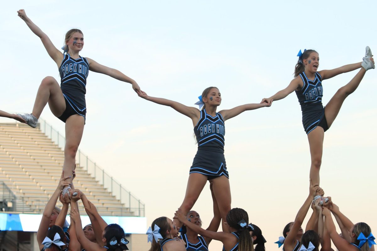 Soaring through the air, the three cheerleaders stand tall and proud during their performance. 