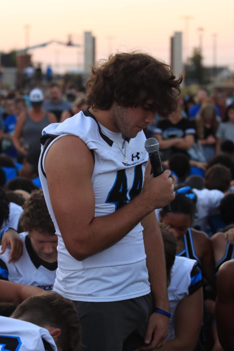 While bowing down his head and holding a microphone in his hands, senior Jonah Bowman prays in company with the audience. 