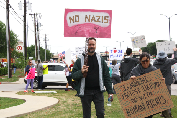 A protester holds a pink sign reading “NO NAZIS” while a woman next to him holds a sign that says “IGNORE THIS PROTEST LIKE YOU DO WITH HUMAN RIGHTS,” calling attention to ongoing human rights concerns.