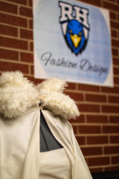 A mannequin dressed in a cream-colored blouse and flowing shawl stands on display in front of the Rock Hill Fashion Design sign. 
