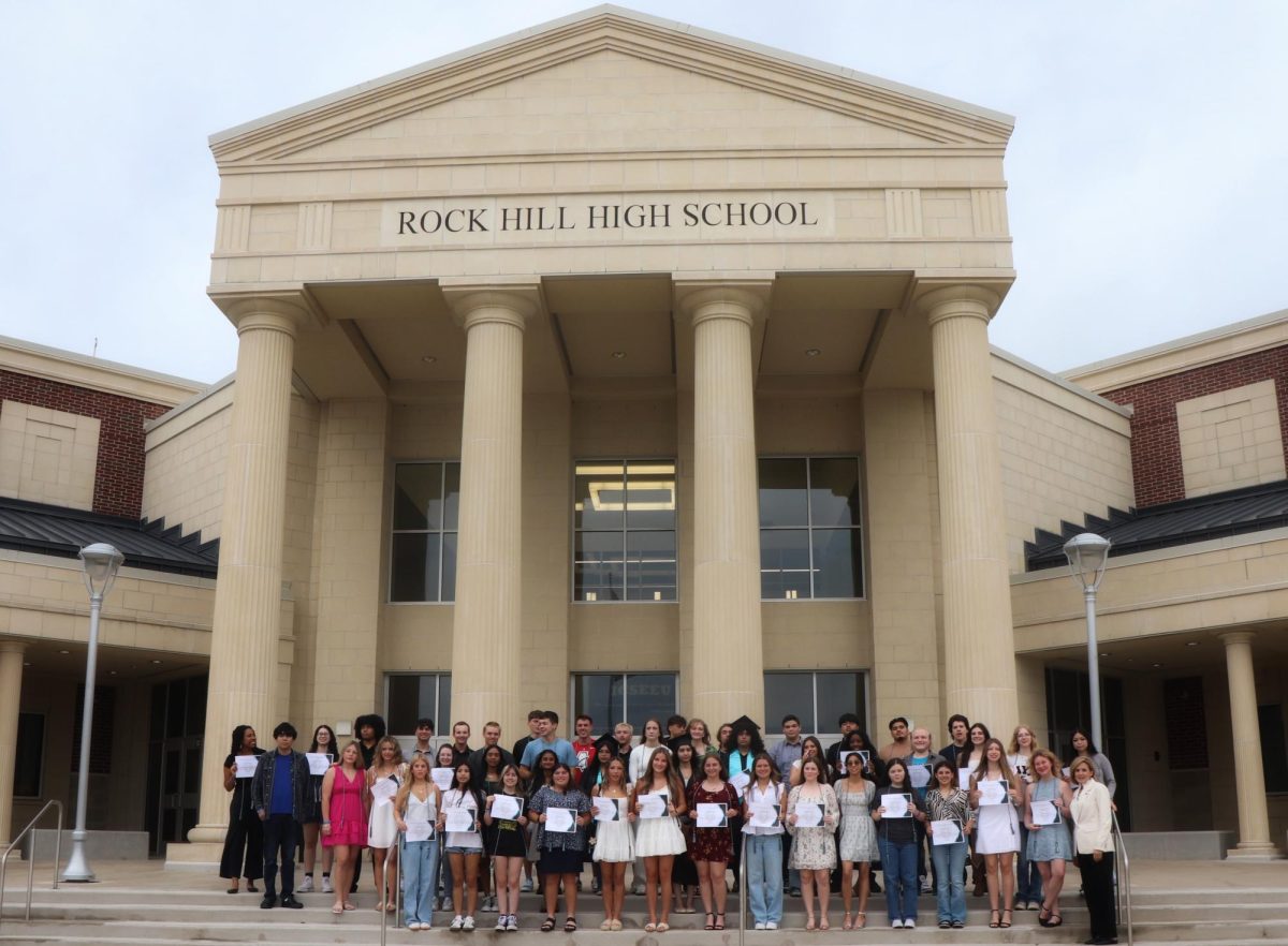 Recognized students show their certificate of recognition and stand in front of the school building.
