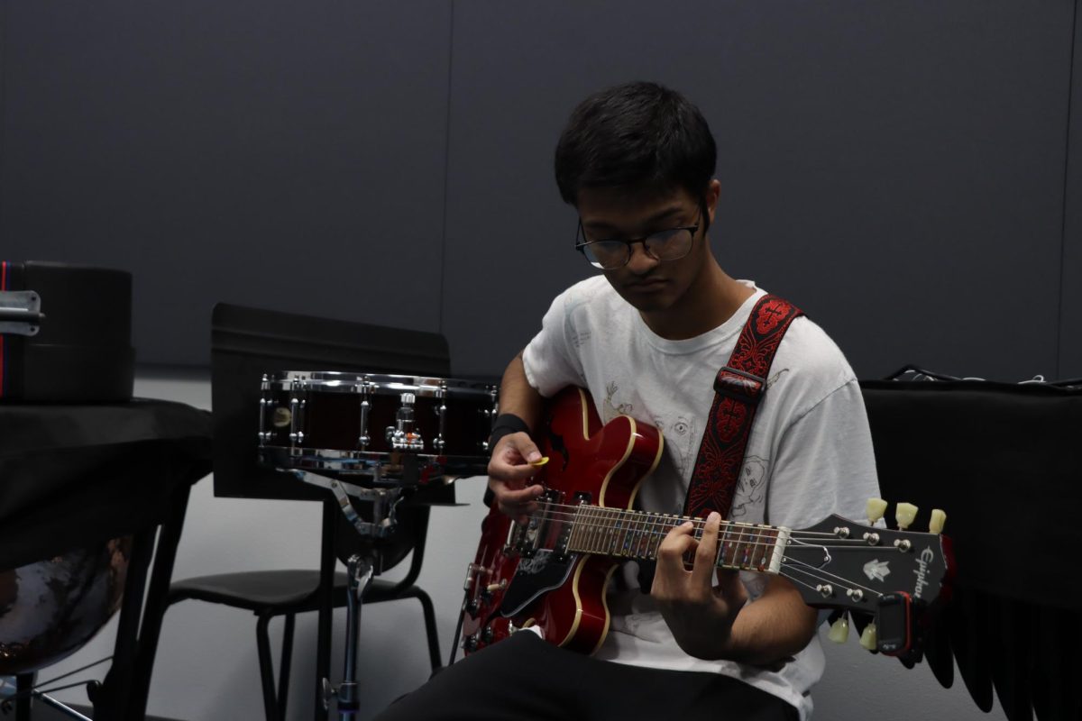 Senior Kareef Khan strumming his guitar in the practice room.